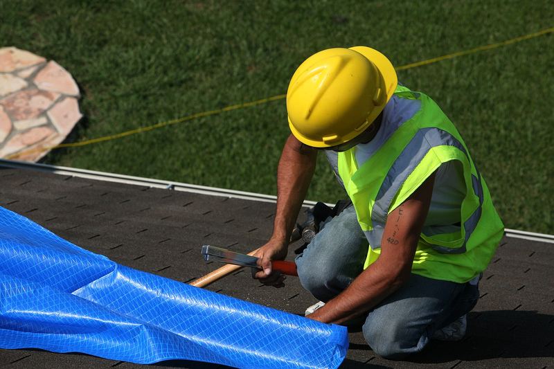 Worker installing a blue tarp on a roof